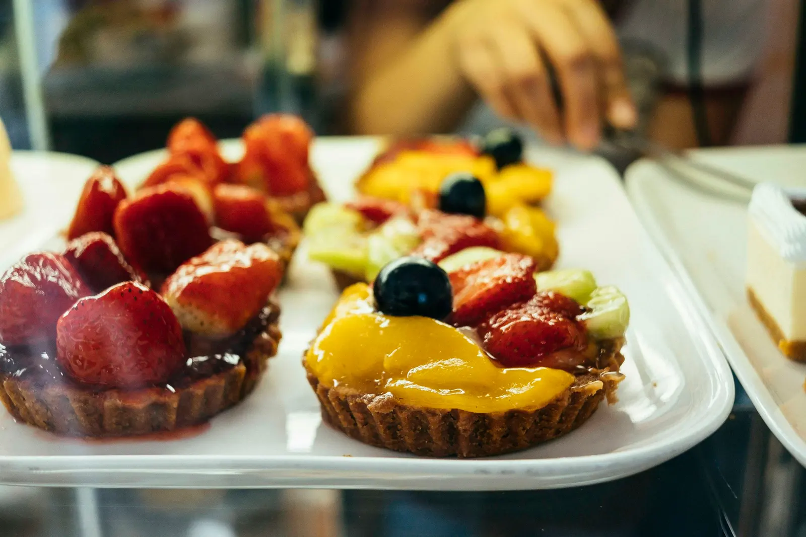Bandeja metálica con tartaletas de fresa, durazno y kiwi en el mostrador de una pastelería.