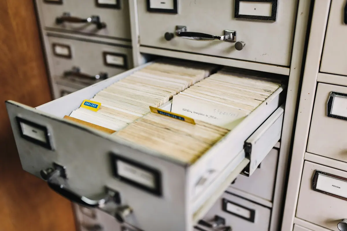 Cajón abierto de un archivador metálico lleno de fichas de cartulina apretadas, con dos separadores de color sobresaliendo entre ellas.
