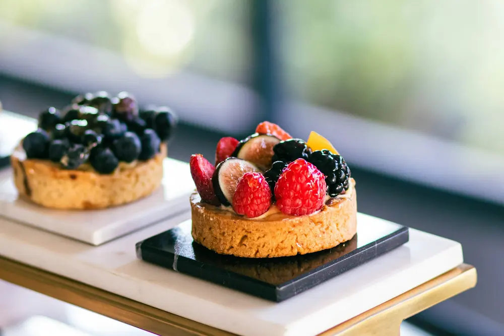Dos tartaletas de masa quebrada con crema y fruta fresca encima, cada una sobre su base de cartón.
