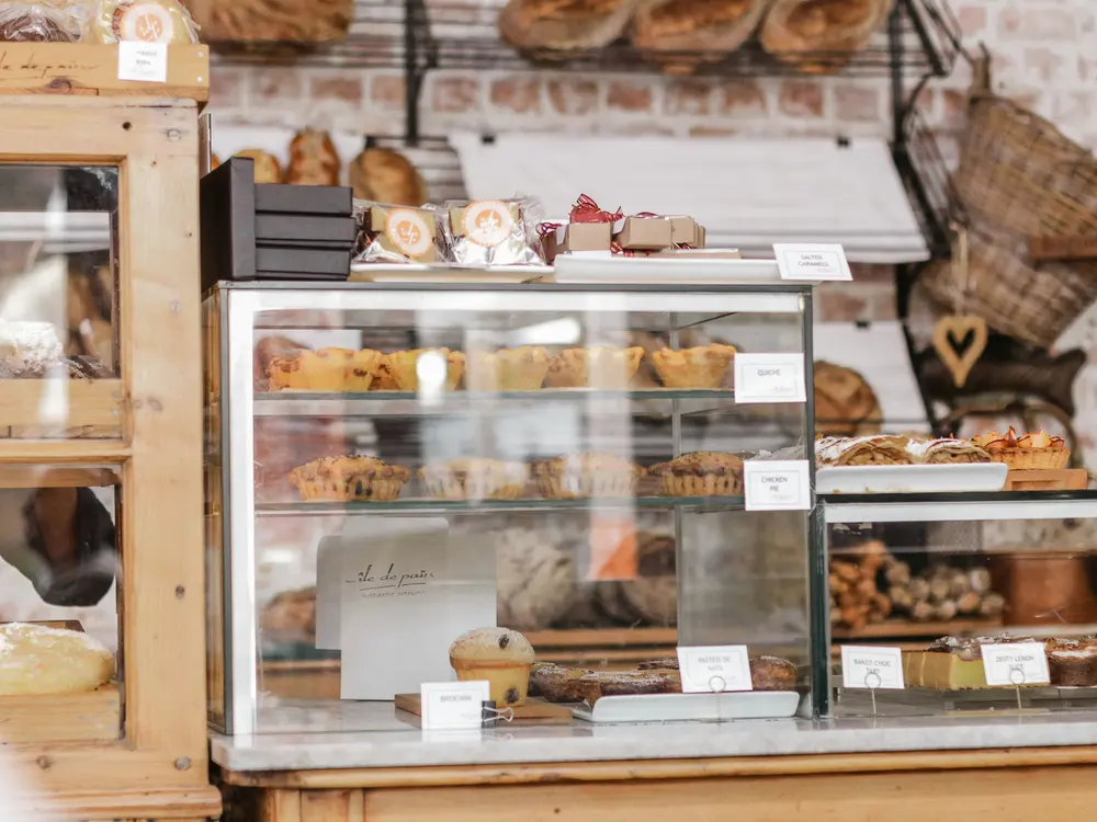 Vitrinas de madera y vidrio de una pastelería con bandejas de pasteles y tarjetas de precio escritas a mano.